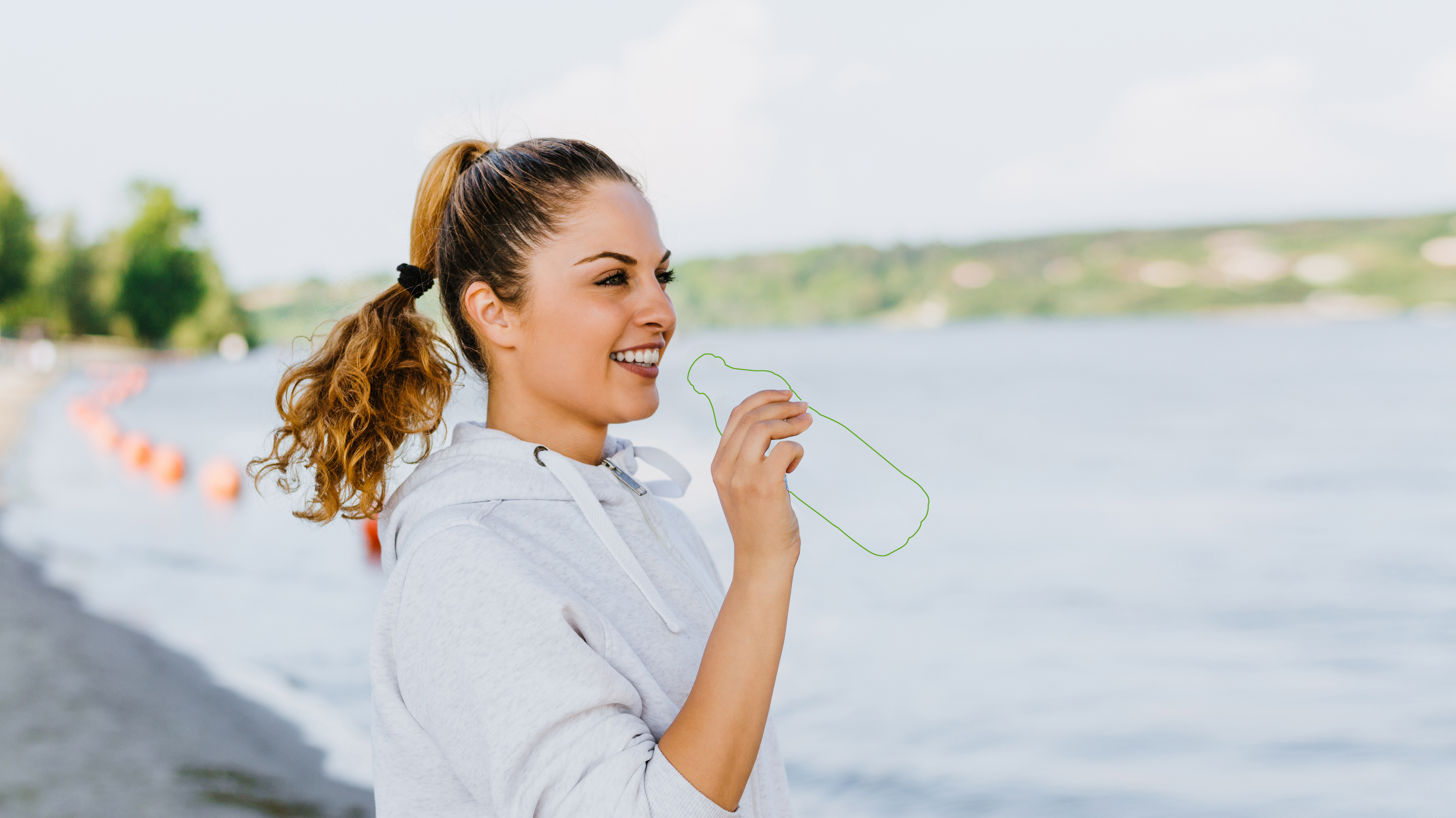 GreenGrafX recycelbares Fotopapier - sportliche Frau mit weißem Hoodie und weg retouchierter Plastikflasche vor einem See im Hintergrund