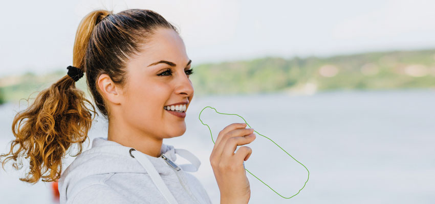 Frau mit weißem Hoodie und angedeuteter Plastikflasche vor einem See